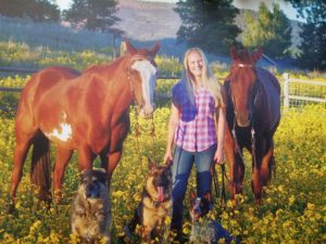 Dr Bruchman posing with her 2 horse, and 3 dogs in a field of flowers