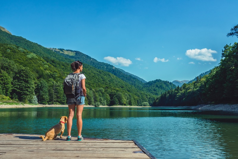 woman and dog standing at a reservoir during a hike in the mountains